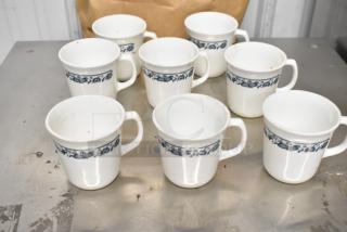 Eight white ceramic mugs with a blue floral band, gently used condition, ideal for kitchen use.