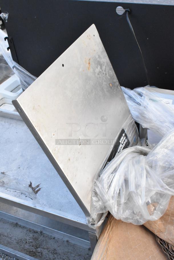 Stainless steel 2-tier over shelf with visible wear and scratches, packed with plastic wrap. No visible tags or labels.