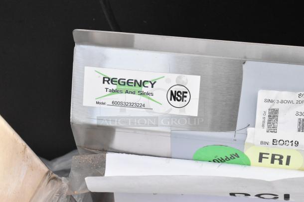 BRAND NEW SCRATCH AND DENT Regency stainless steel 3-bay sink, model 600S32323224, with dual drain boards, no legs. Tags show NSF certification.