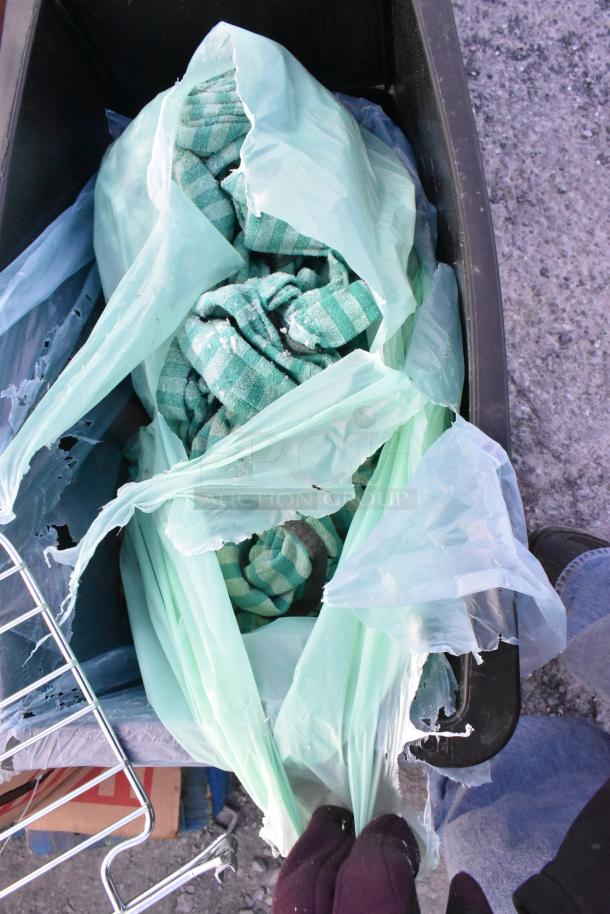 Black Poly Slim Jim trash can filled with contents, including a green striped fabric and torn plastic bags. Usual wear visible.