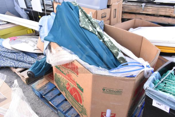 Lot of assorted patio umbrellas in a cardboard box on a pallet. Various colors and patterns. Mixed condition.