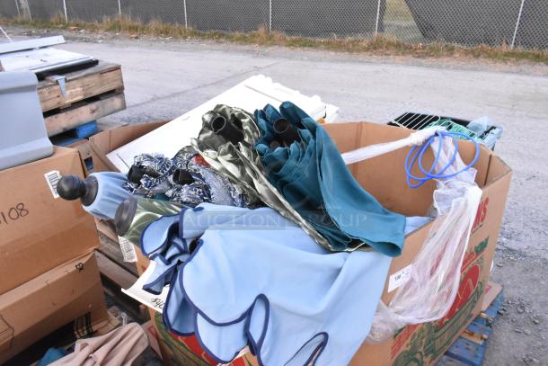 Lot of assorted patio umbrellas in various colors and patterns, folded, placed in a cardboard box; suitable for outdoor use.