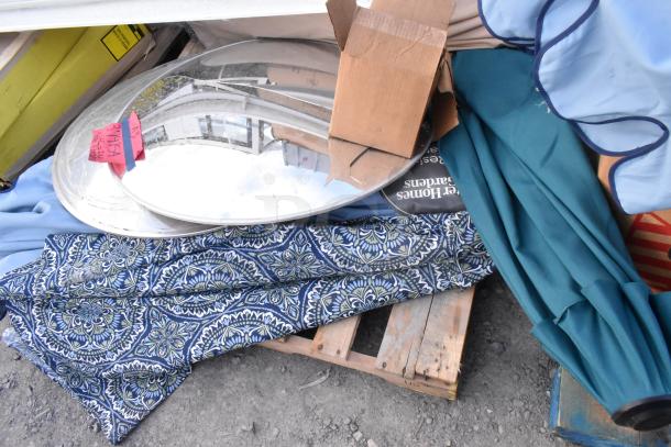 Various items including oval mirrors and patio umbrellas, some with floral fabric, on a wooden pallet. Tags with lot numbers visible.
