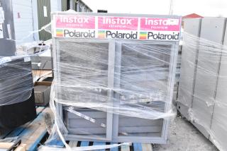 Gray metal cabinet wrapped in plastic, featuring "Instax Fujifilm" and "Polaroid" labels on top, indicating potential retail use.