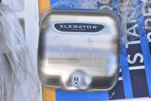 Xcelerator hand dryer in brushed metal, showing "Xcelerator" and "Feel the Power" labels. Slight surface wear visible.
