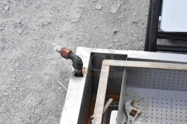 Metal grease trap on commercial casters with perforated interior. Visible rust and wear indicate moderate use.