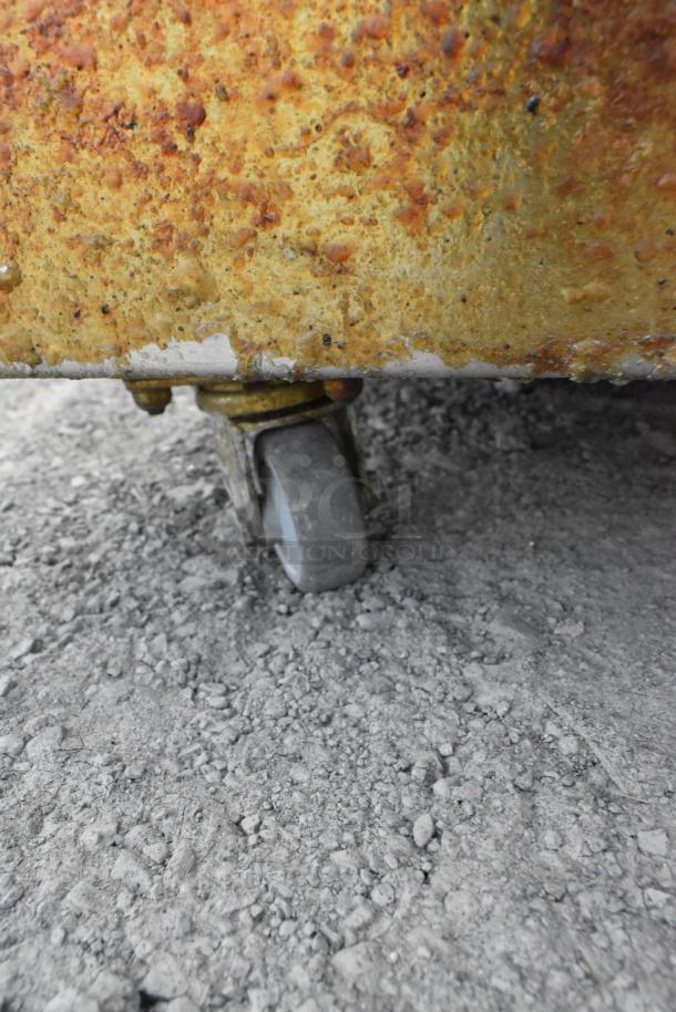 Metal grease trap with rusty surface on commercial caster wheel, showing heavy wear, offering mobility and durability.