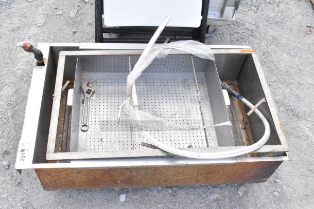 Metal grease trap with perforated interior tray, visible rust, and commercial casters. Includes attached piping and tools.
