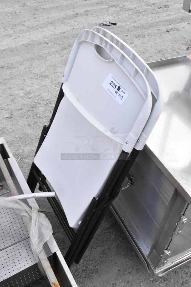 Two white poly and metal folding chairs, durable, lightly used. Auction label: "225 + x2". Ideal for events.
