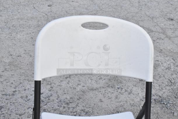 White folding chair with poly seat and back, metal frame; visible wear, ideal for events.