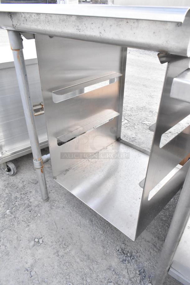 Stainless steel commercial dishwasher table with over shelf and under shelf, showing sturdy construction and slight wear.