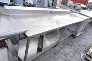 Stainless steel table with metal under shelf and back splash, industrial design, good condition, minimal wear visible.