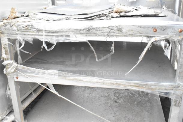 Stainless steel equipment stand with battered surfaces and torn packaging, indicating heavy use and wear.