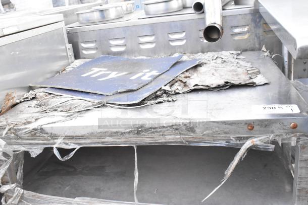 Stainless steel equipment stand, used condition, surface wear and signs of rust. Visible paper debris and metal pipes on top.