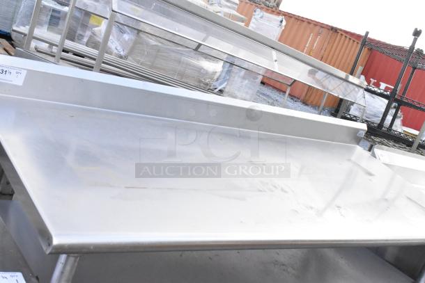 Stainless steel commercial table with two under shelves and backsplash, used condition, label visible with auction details.