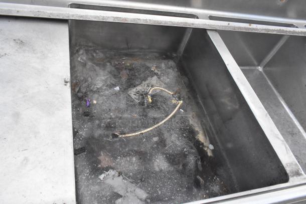 Stainless steel 3 bay sink with dual drain boards, showing signs of wear and debris inside, indicative of used condition.