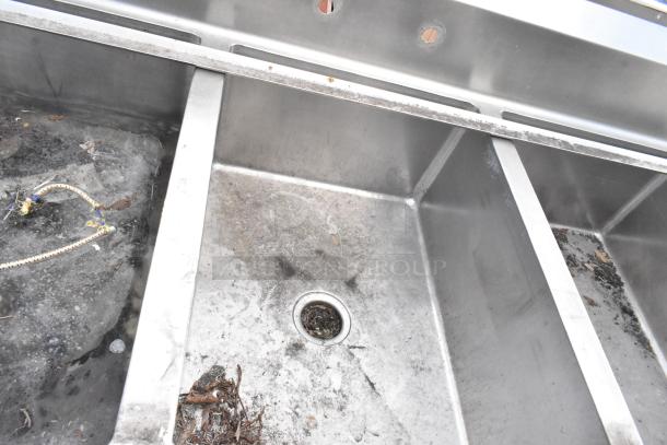 Stainless steel 3 bay sink with dual drain boards. Visible wear and debris indicate used condition. No visible tags or markings.
