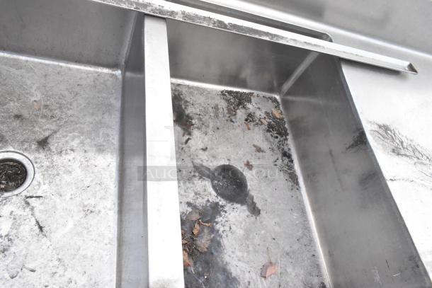 Stainless steel 3 bay sink with dual drain boards, showing signs of use and minor debris. Ideal for commercial settings.