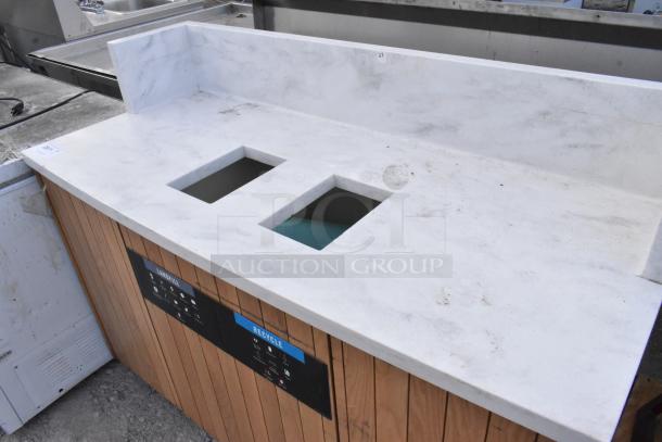 Trash can shell with two deposit holes and doors, featuring a marble-like top and wood paneling. Marked for landfill and recycling.