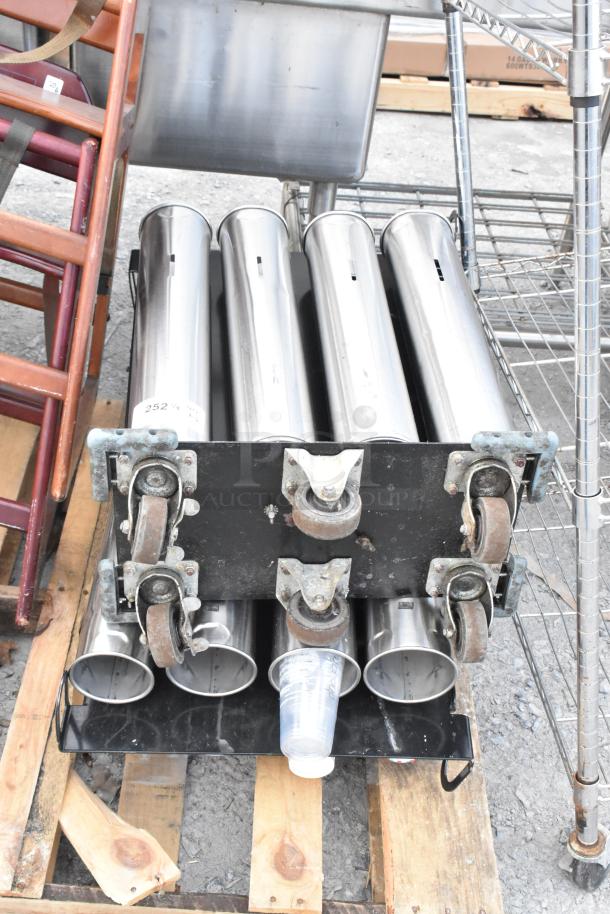 Wooden high chair and metal cup dispenser on a pallet. High chair has visible wear. Cup dispenser includes plastic cups.