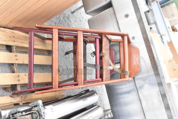 Wooden high chair with safety straps, showing minor wear, stacked on industrial equipment near a metal cup dispenser. Auction item tag attached.