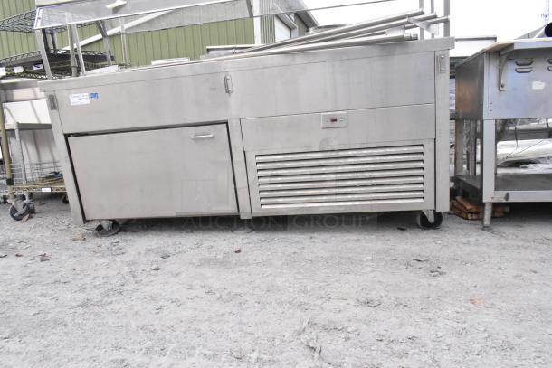Stainless steel commercial buffet station with sliding doors, on commercial casters for mobility. Signs of outdoor wear.