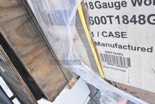 Stack of boxed scratch and dent commercial tables, labeled 600T1848G, wrapped in plastic, wooden palettes visible.