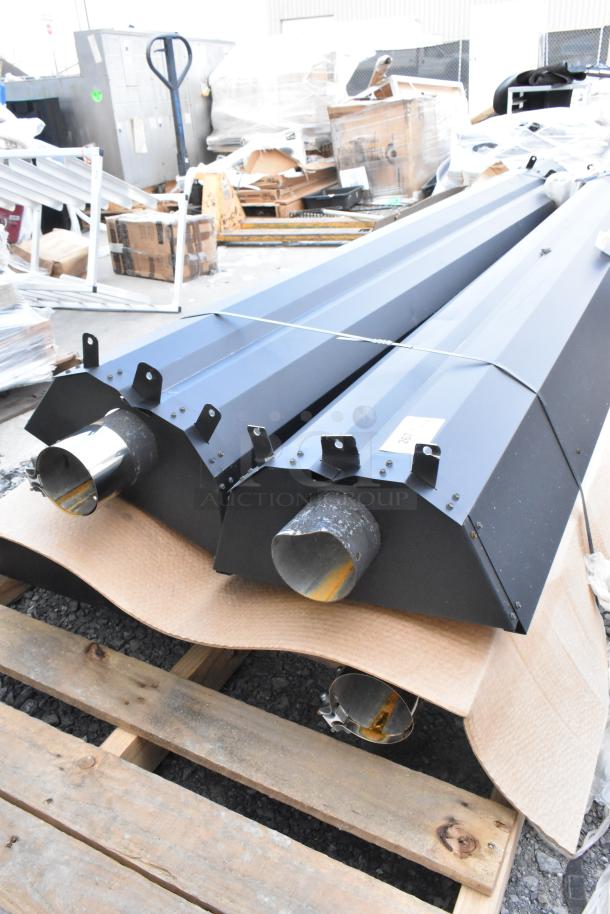 Four brand new black metal pieces on a pallet, scratch and dent condition, with mounting brackets and pipe fittings.