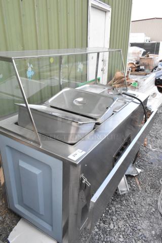 Stainless steel 4-bay electric steam table with sneeze guard, tray slide, and inserts. Used condition, visible wiring.