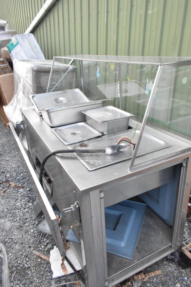 Stainless steel 4 bay electric steam table with sneeze guard, tray slide, and inserts; visible wiring and controls; fair condition.