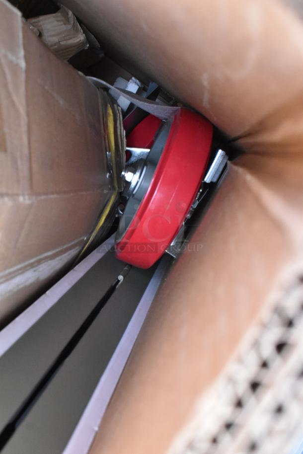 Box containing scratch and dent stainless steel worktables and equipment stands, partially visible with red caster wheels.
