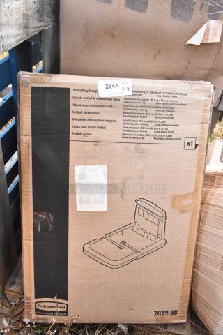 Box of Rubbermaid commercial products, including a vertical baby changing station. Brown cardboard with product illustrations and specs.