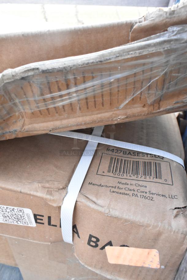 Boxes of assorted new items, including a Lancaster Table 42" MDF tabletop and 50 lb. steel umbrella base, with visible wear.