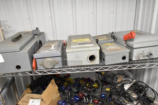 Five assorted used power boxes on a metal shelf, various models and sizes, some with attached red levers and labels.