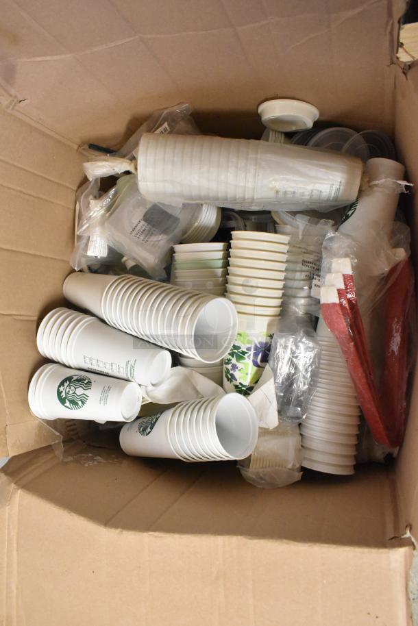 Box of assorted items including paper Starbucks cups and red tongs. Various cup sizes and floral designs visible.