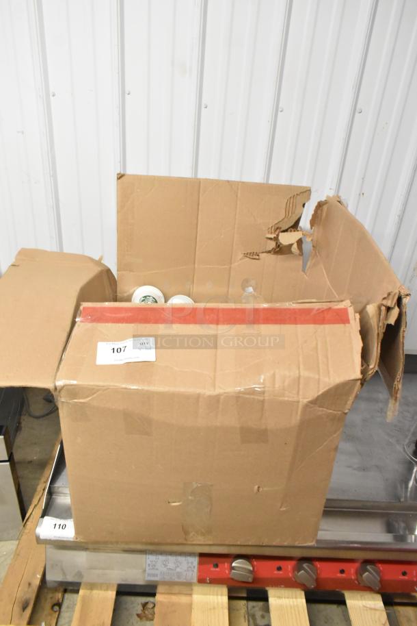 Cardboard box with various items, including paper Starbucks cups and tongs, showing wear. Label reads "107 QTY: lot."
