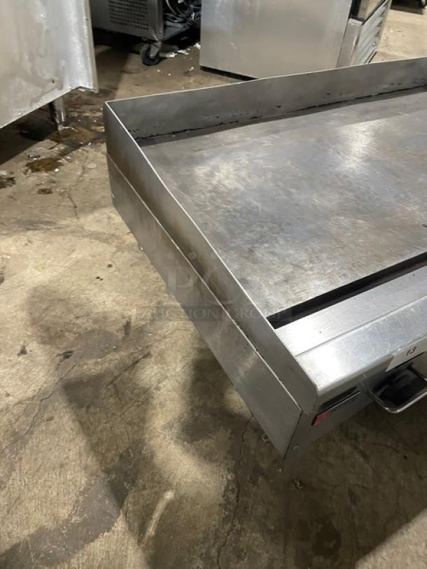 Wolf commercial stainless steel gas griddle with back and side splash, on legs. Sturdy and suitable for heavy-duty use.