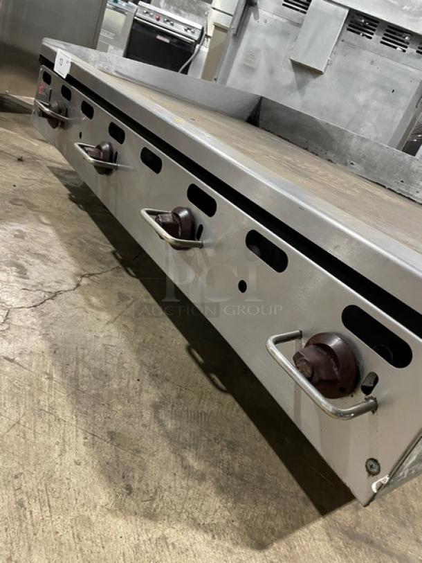 Wolf commercial stainless steel gas countertop flat griddle with back and side splash, on legs. Four control knobs visible.
