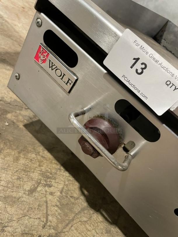 Wolf commercial stainless steel gas countertop griddle with back and side splash, on legs. Featuring a visible brand logo and control knob.