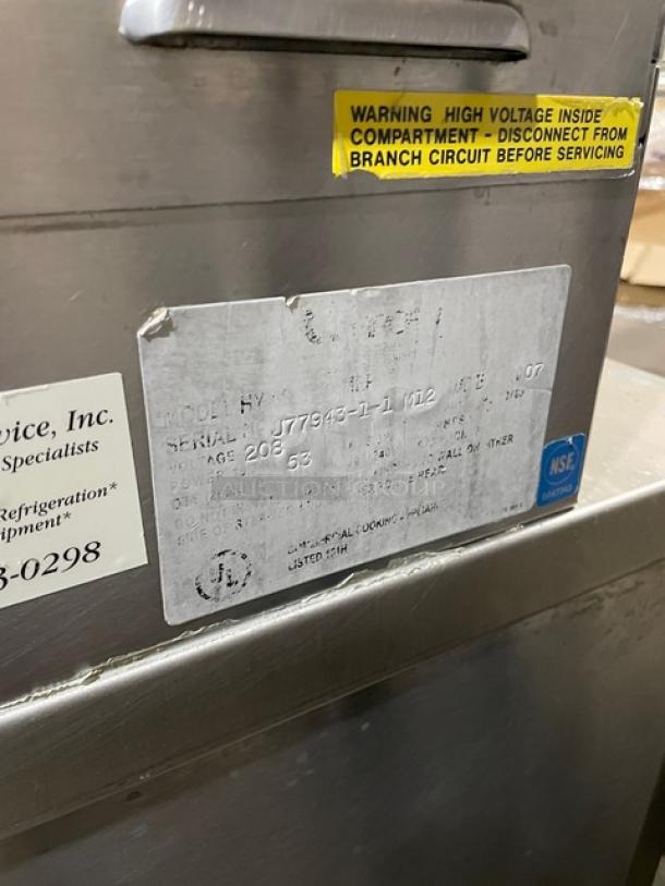 Groen HY-6E commercial stainless steel double compartment convection steamer with individual controls, built-in pan racks, serial number J77943-1-1 M12, 208V, on bullet feet legs. Warning label indicates high voltage.