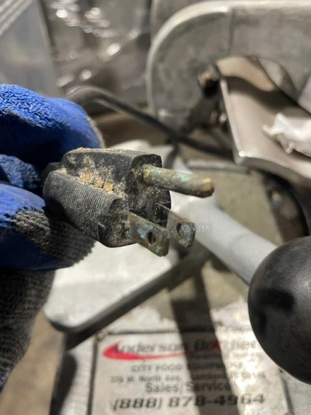 Aging electrical plug of a Hobart VCM40 commercial mixer, slightly corroded, held with a gloved hand.