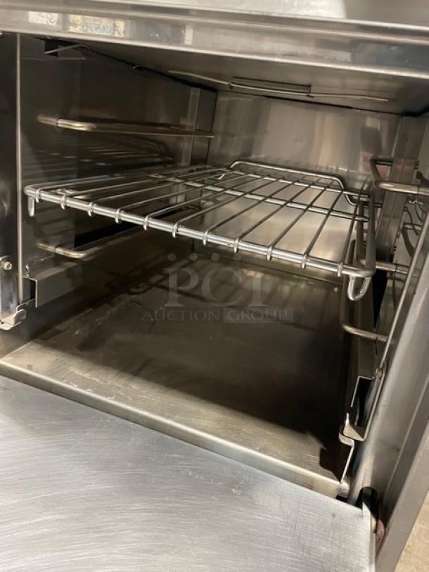 Jade Range JBR424 commercial stainless steel gas-powered 4-burner range/oven combo with wired oven rack, on legs.