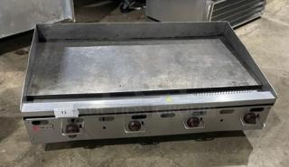 Wolf commercial stainless steel gas griddle with back and side splash, four control knobs, and sturdy legs; ideal for heavy-duty cooking.