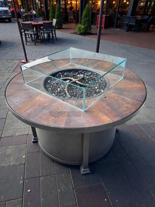 Round gas fire pit table by Outdoor Living in pristine condition, suitable for natural gas or propane, featuring glass wind guard.