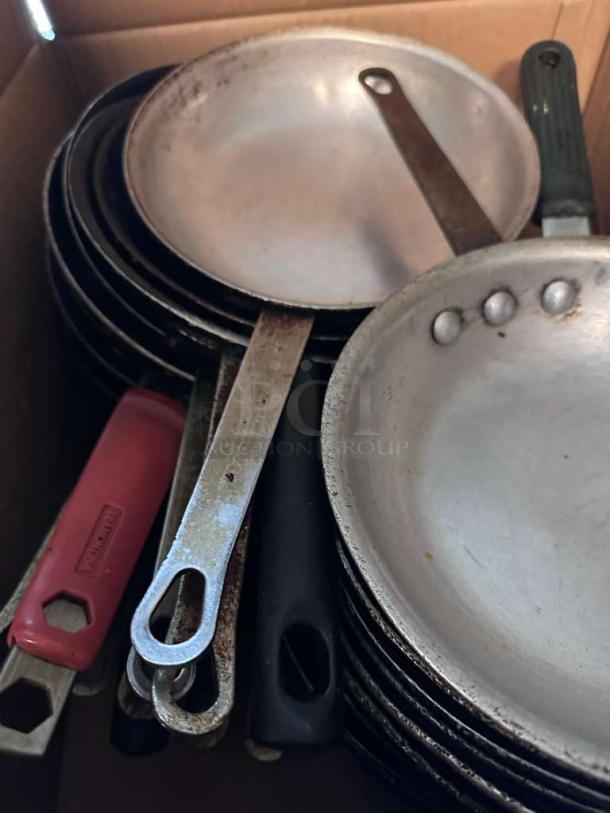 Approximately 30 commercial frying pans from mixed brands, clean and heavy-duty, stacked in a box, ready for use.