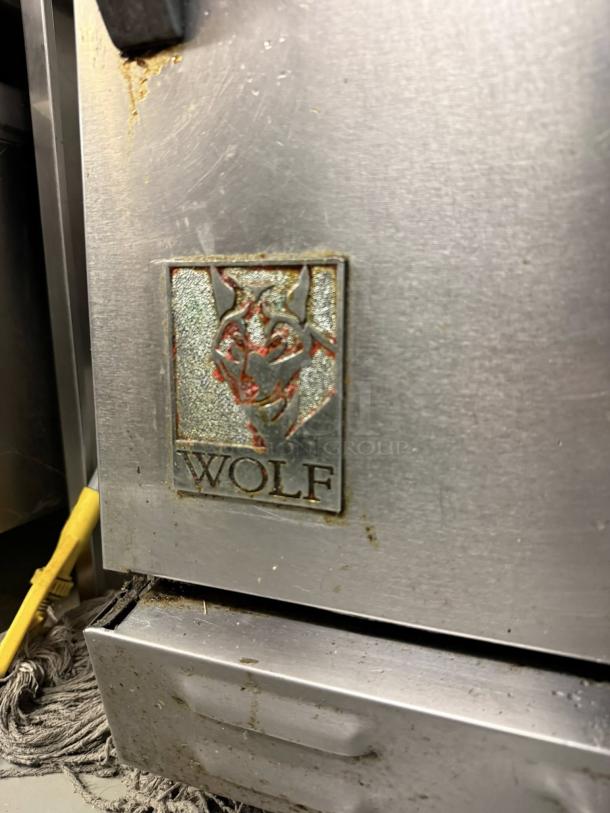Wolf C36S-36G commercial gas range with full griddle and oven. Features “Wolf” logo on stainless steel surface.