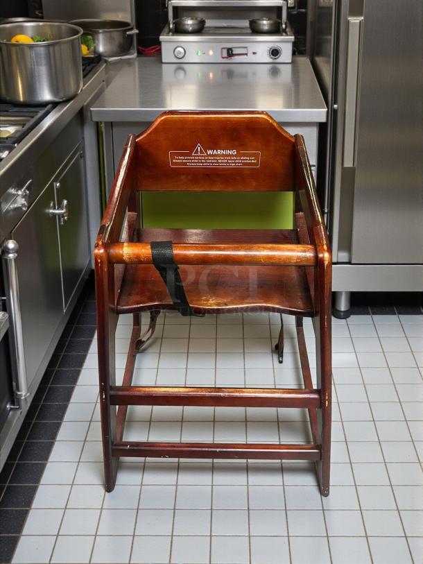 Modesto high chair in brown wood finish, pristine condition, sturdy construction, safety warning label visible on back.