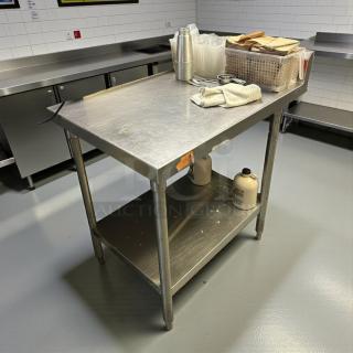 Stainless steel work table with backsplash by Omniteam; sturdy, tested, and in refined condition. Features under-shelf storage.