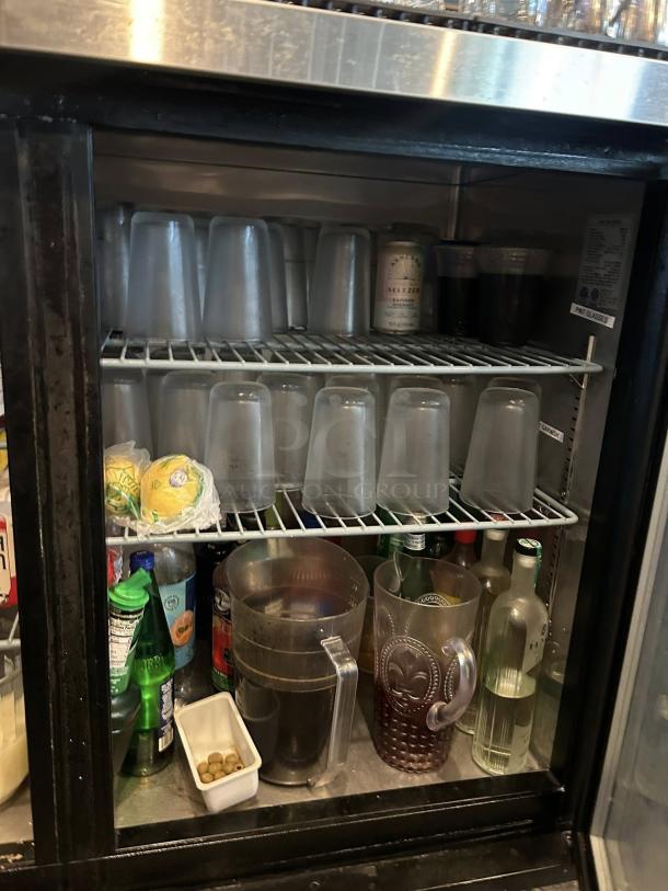 Dukers DBB60-H2 two-section glass door back bar cooler, pristine condition, containing assorted beverages and glasses.