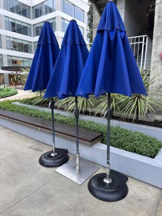 Three blue commercial-grade outdoor patio umbrellas in immaculate condition with heavy-duty bases, ready for use.